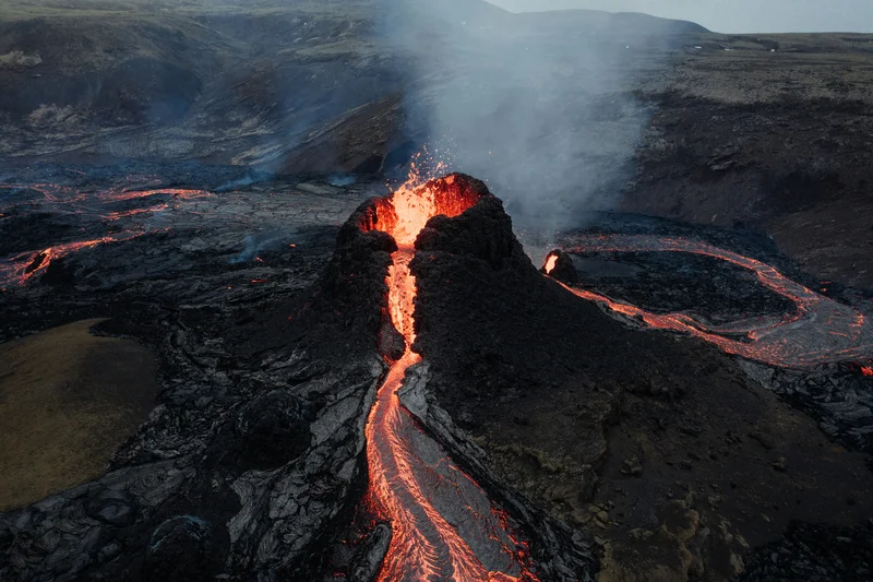 Glowing lava flowing across dark volcanic rock beneath a cloudy sky.