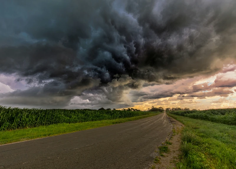 Dark storm clouds gathering above a rural road bordered by green fields.