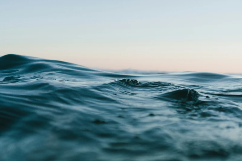 Close-up view of gentle blue ocean waves beneath a pale sky.